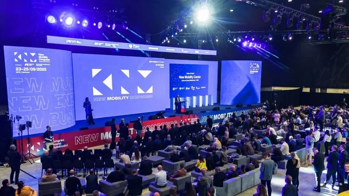 Prelegent na scenie New Mobility Congress przed dużymi ekranami, liczni uczestnicy siedzą i stoją.