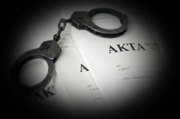Metalowe kajdanki leżą na dokumentach z napisem „AKTA”.
