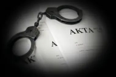 Metalowe kajdanki leżą na dokumentach z napisem „AKTA”.