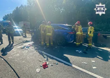 Strażacy interweniują przy rozbitym niebieskim samochodzie na drodze, na miejscu są też policjanci.
