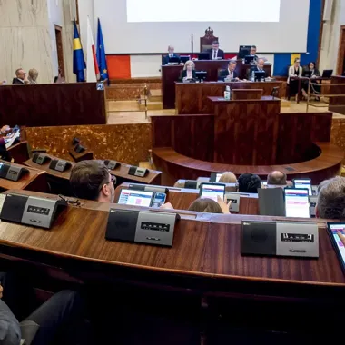 Posiedzenie w auli uczelni lub sali sejmowej z uczestnikami przy drewnianych ławach wyposażonych w tablety i mikrofony, na podium siedzą przedstawiciele władz.